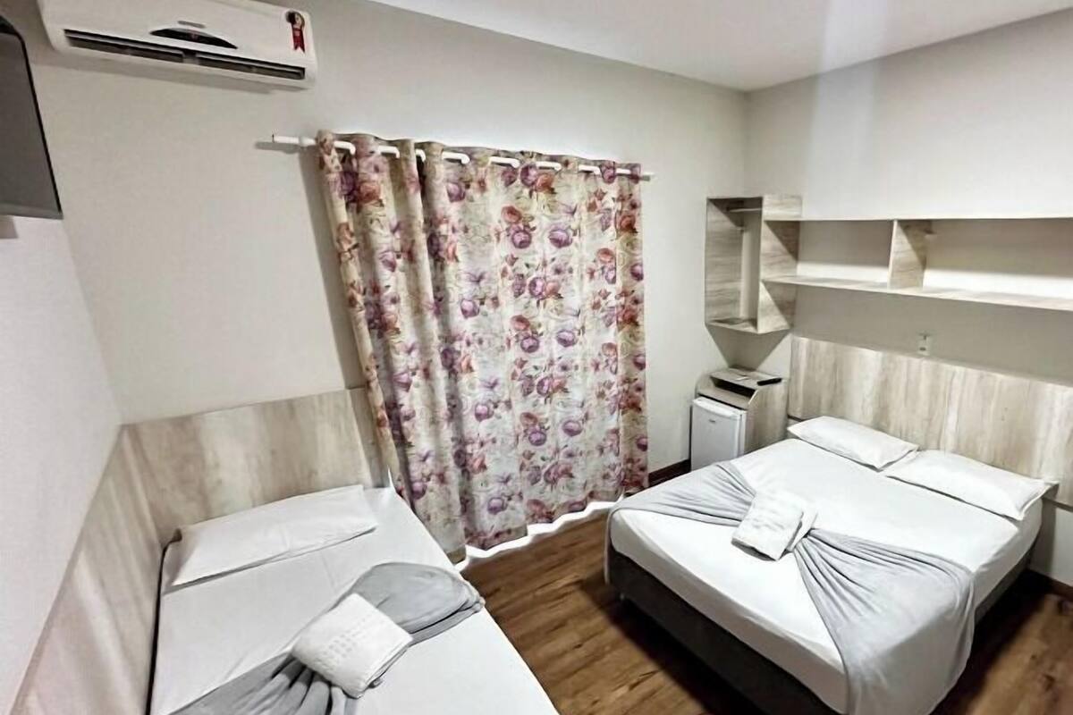 A hotel room with two beds, a wooden floor, a shower area, and a built-in shelf.