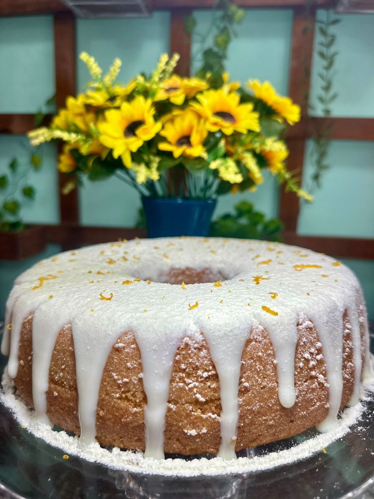 Un gâteau en forme de couronne, recouvert d’un glaçage blanc, présenté sur un présentoir en verre.