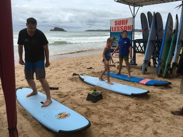 Una playa con tablas de surf y un cartel que dice 'SURF LESSON'.
