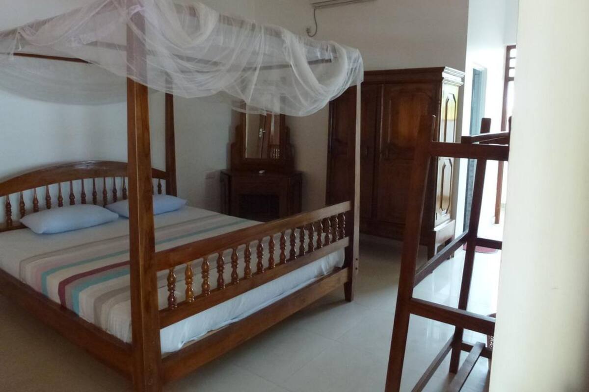 A four-poster bed with a canopy, a wooden dresser, and a mirror.