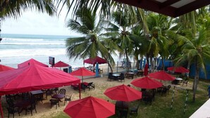 A beachside restaurant with red umbrellas and tables, overlooking the ocean. - Samaru Beach House (Weligama)