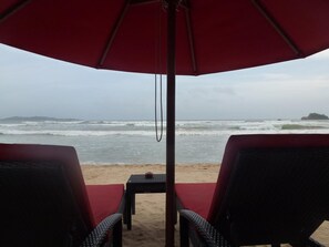 A beach view with a red umbrella, two wicker chairs, and a small table. - Samaru Beach House (Weligama)