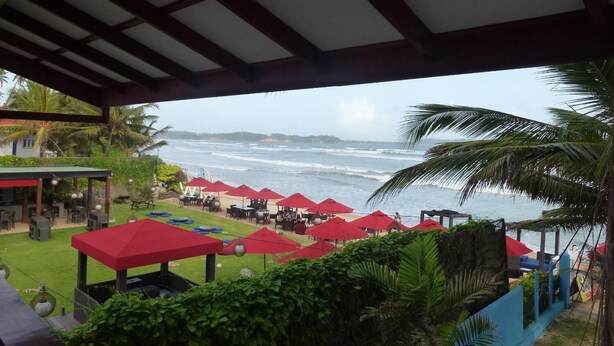 A beachside restaurant with outdoor seating and red umbrellas, overlooking the ocean. - Samaru Beach House (Weligama)