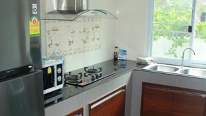 A modern kitchen with a stainless steel refrigerator, a gas stove, wooden cabinets, and a window with a view of greenery. - Pitchayapa Hua Hin Pool Villa Holiday (Hua Hin)