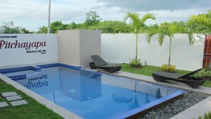 A swimming pool with lounge chairs, a white wall, and greenery in the background. - Pitchayapa Hua Hin Pool Villa Holiday (Hua Hin)