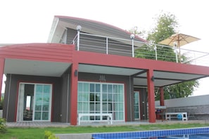 Une maison moderne à deux étages, dotée d’un balcon, d’une piscine et d’un patio couvert.