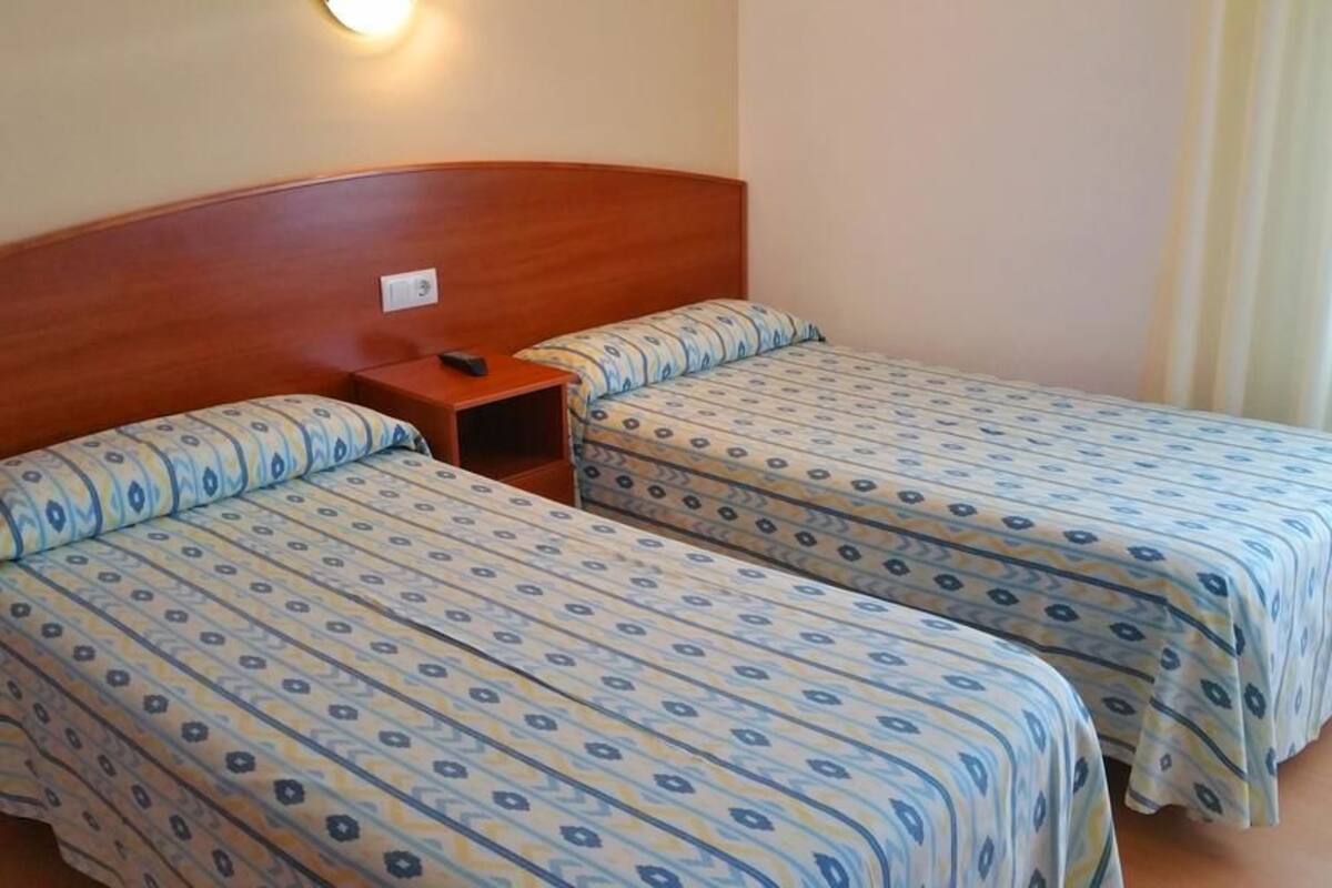 A hotel room with two beds, each with patterned bedding, a wooden headboard, and a bedside table with a remote control.