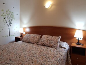 A neatly made bed with floral-patterned bedding, two bedside lamps, and a wall decoration of a tree with birds. - Hostal Mary (Lloret de Mar)