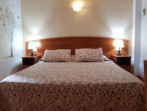 A neatly made bed with a patterned bedspread, two pillows, and two bedside lamps on wooden nightstands. - Hostal Mary (Lloret de Mar)