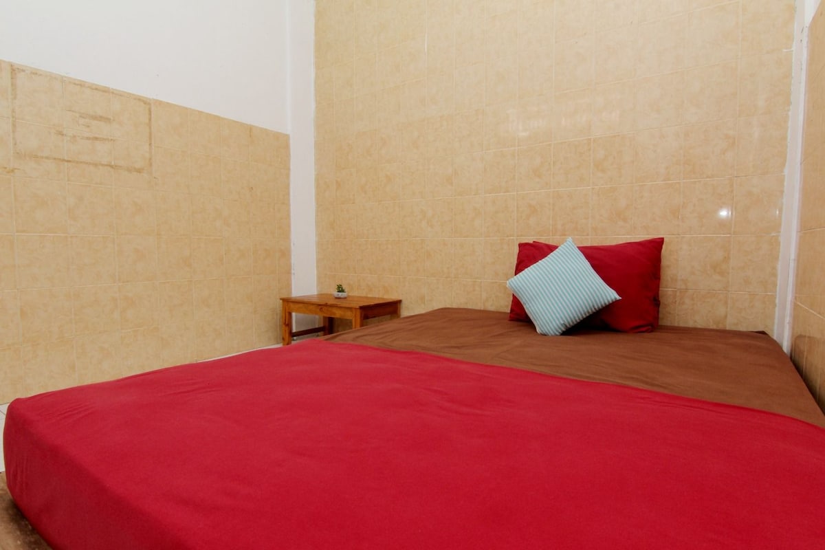 A room with a bed, a small wooden nightstand, and beige tiled walls.