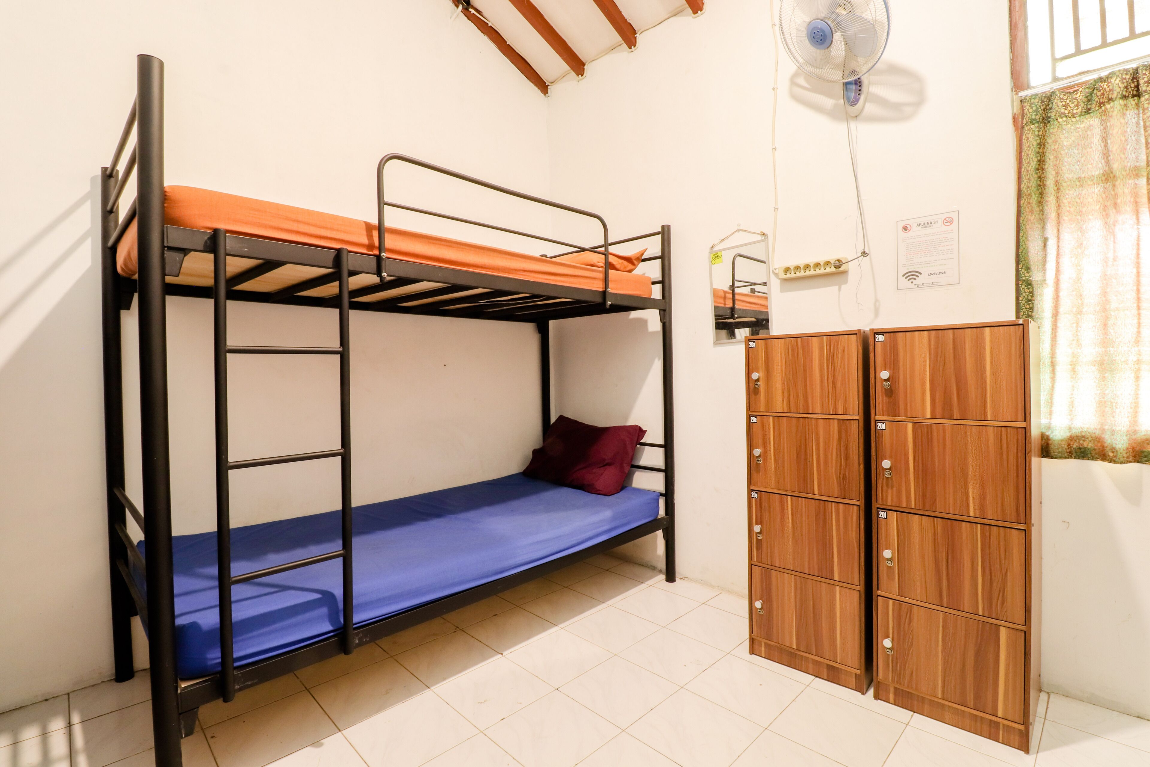 A bunk bed with a blue mattress and orange bedding, a wooden wardrobe, and a ceiling fan.