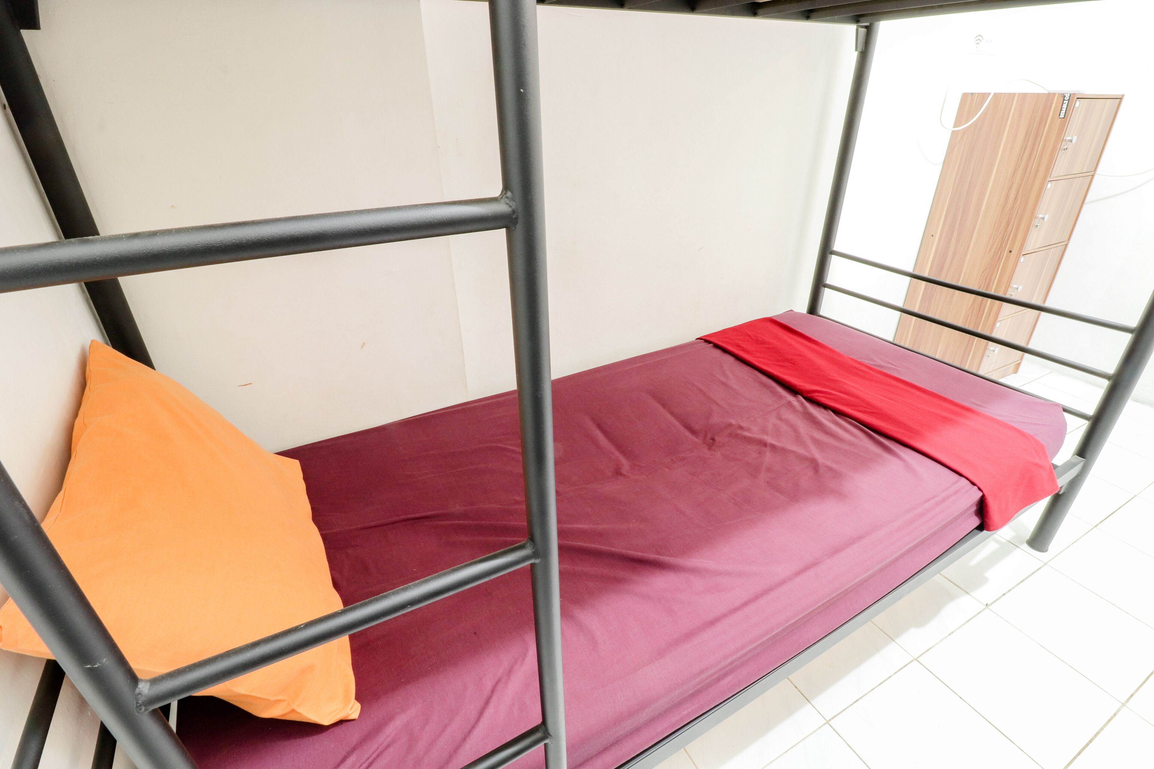 A bunk bed with a red mattress and an orange pillow.