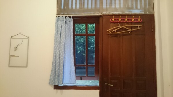 Una habitación con puerta de madera, ventana con vistas a vegetación, un interruptor de luz colgante y un tendedero.
