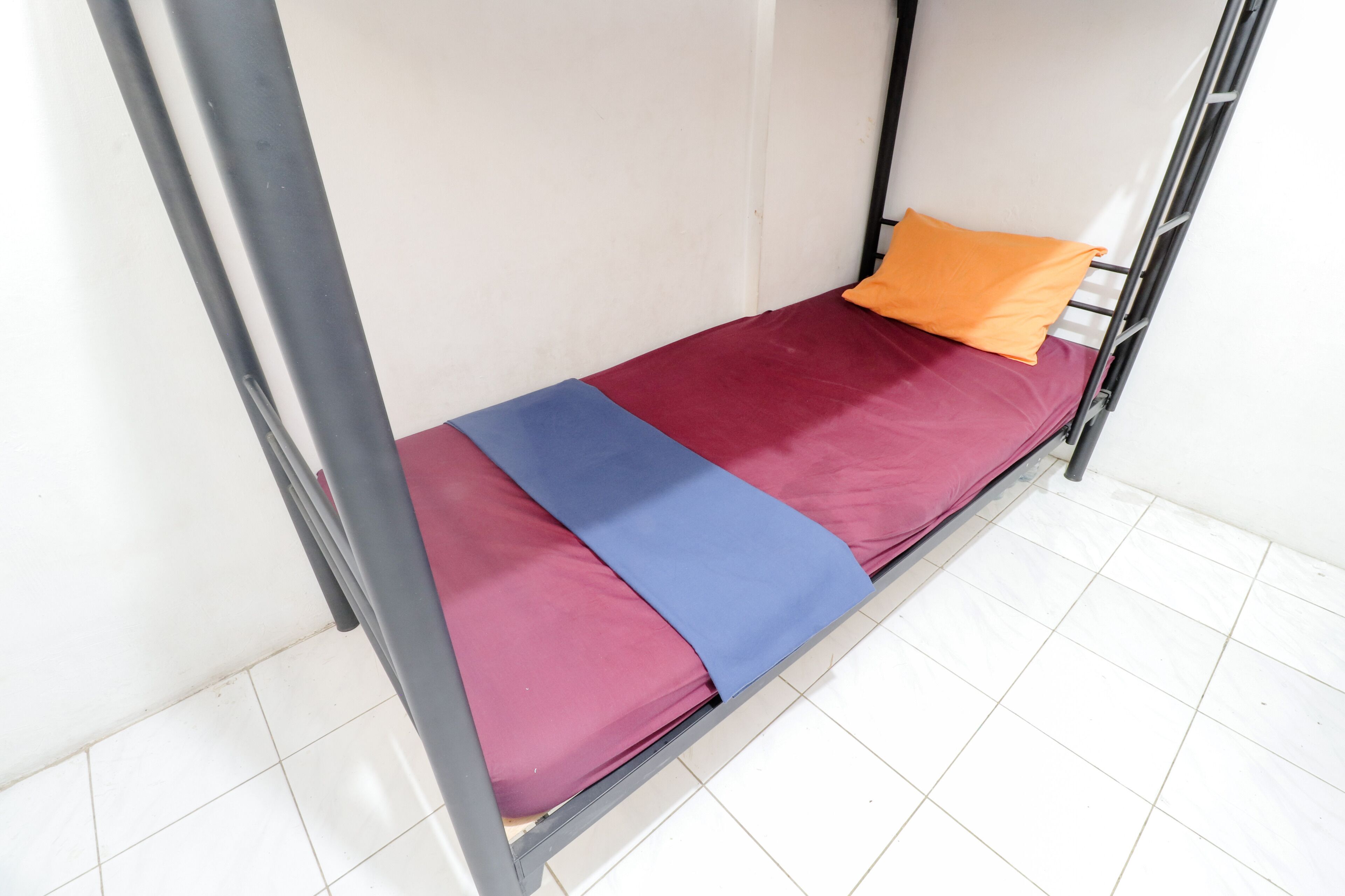 A bunk bed with a blue and red mattress, an orange pillow, and metal railings.