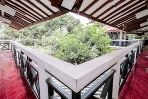 Un espacio al aire libre cubierto con suelo de baldosas rojas, barandilla blanca y vistas a vegetación exuberante.