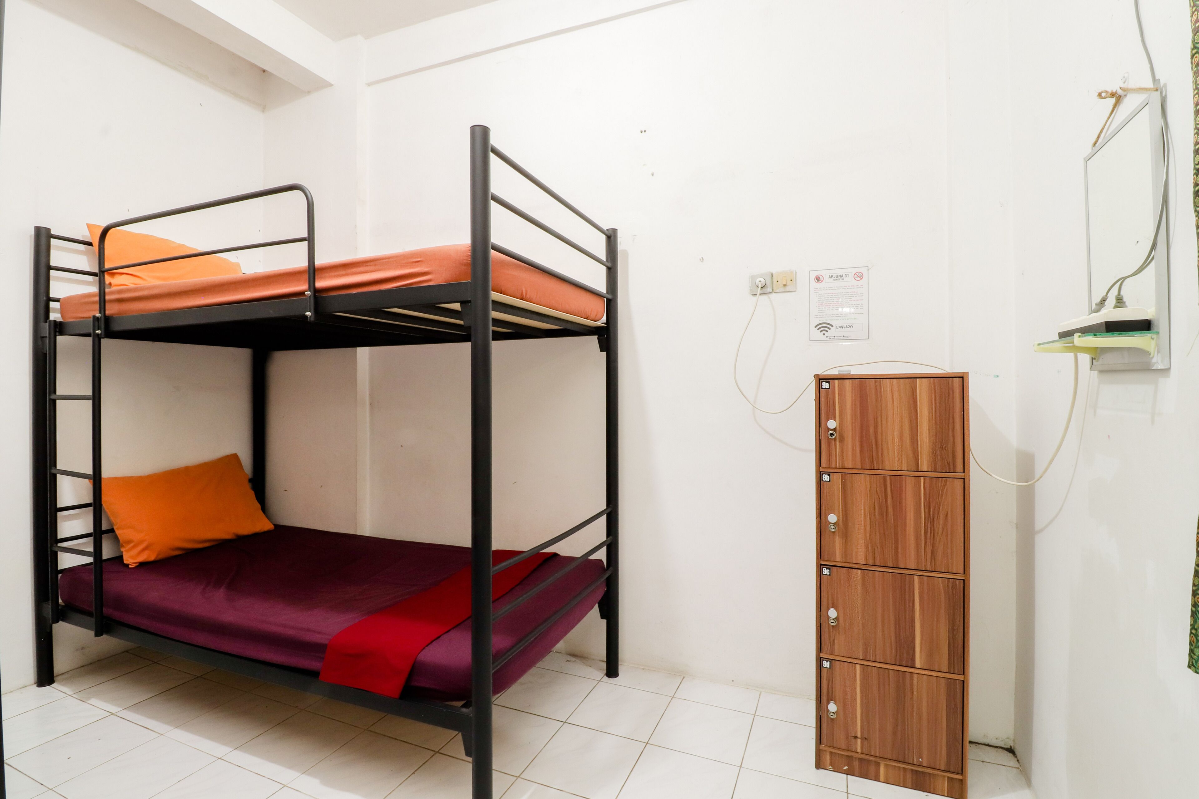 Una cama litera con ropa de cama naranja y roja, un armario de madera y un suelo de baldosas blancas.