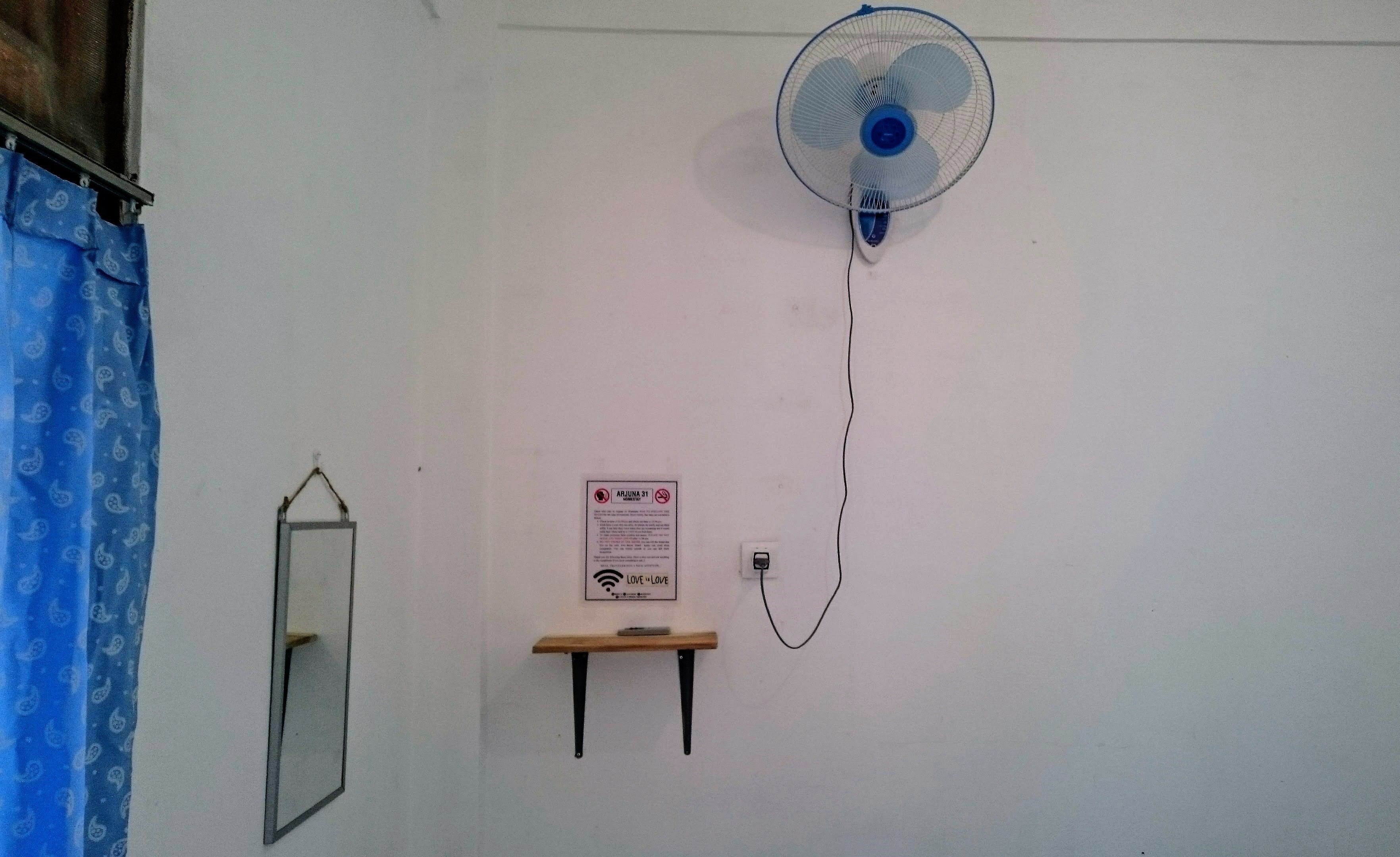 Ein Zimmer mit einem Wandventilator, einer kleinen Ablage mit einem Schild und einem Spiegel.
