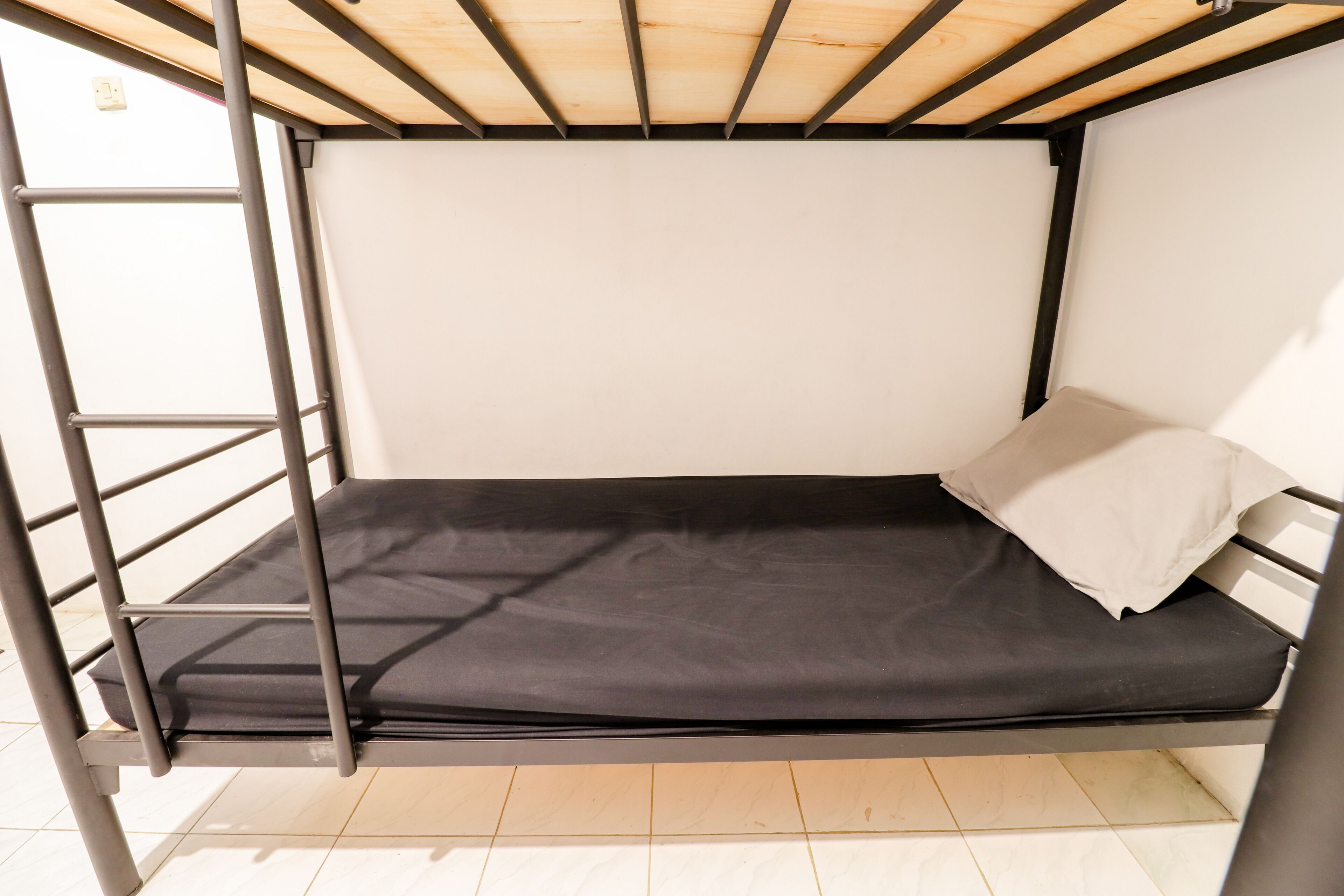 A bunk bed with a black mattress and white pillows, metal frame, and wooden ceiling beams.