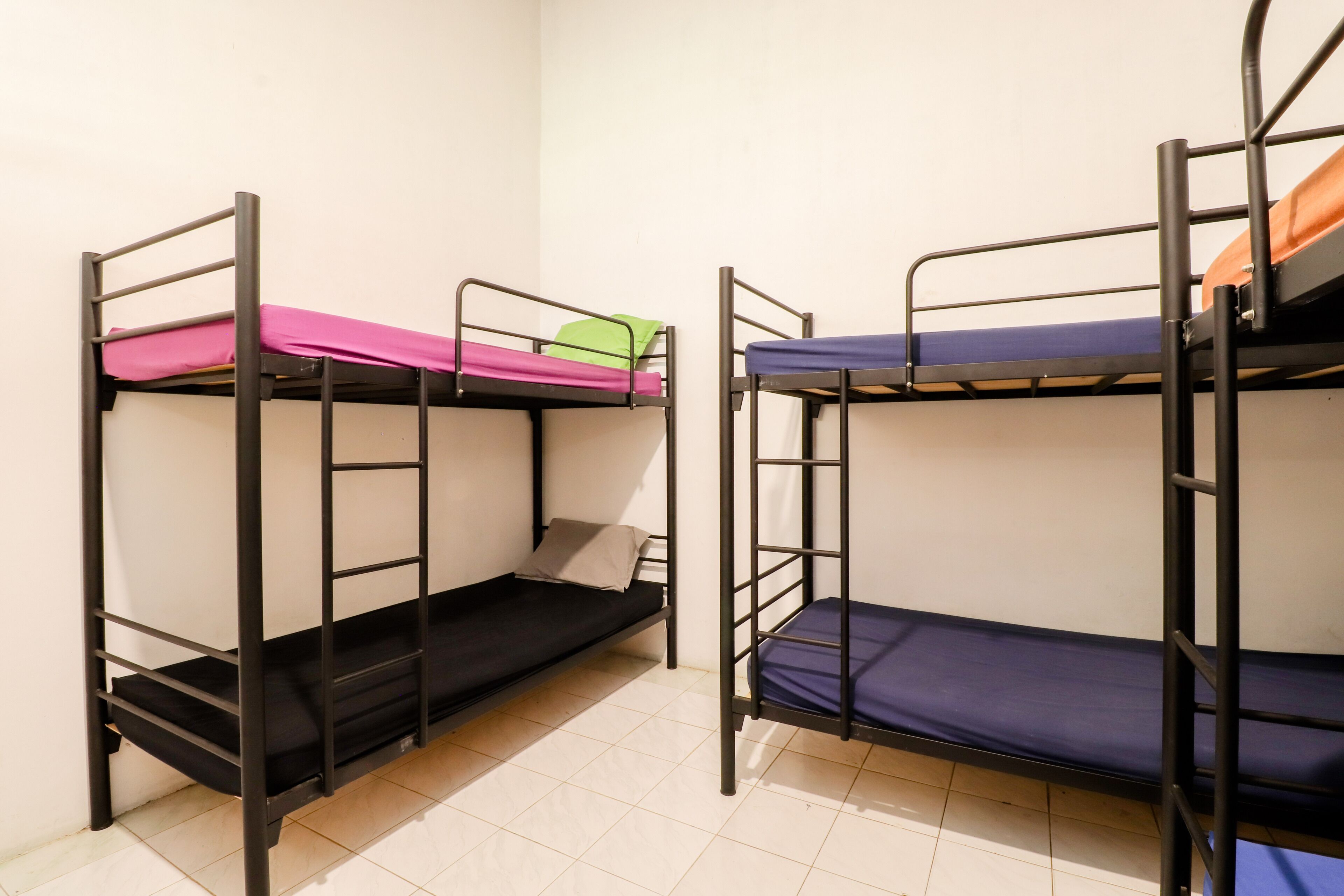 Two bunk beds with different colored bedding in a room with white walls and tiled flooring.