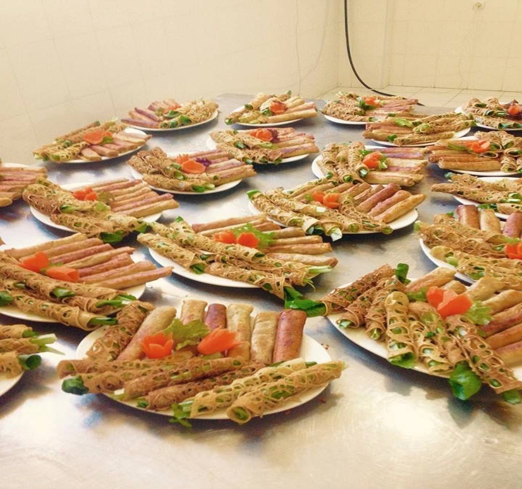 A table with multiple plates of rolled spring rolls and noodles, garnished with vegetables.
