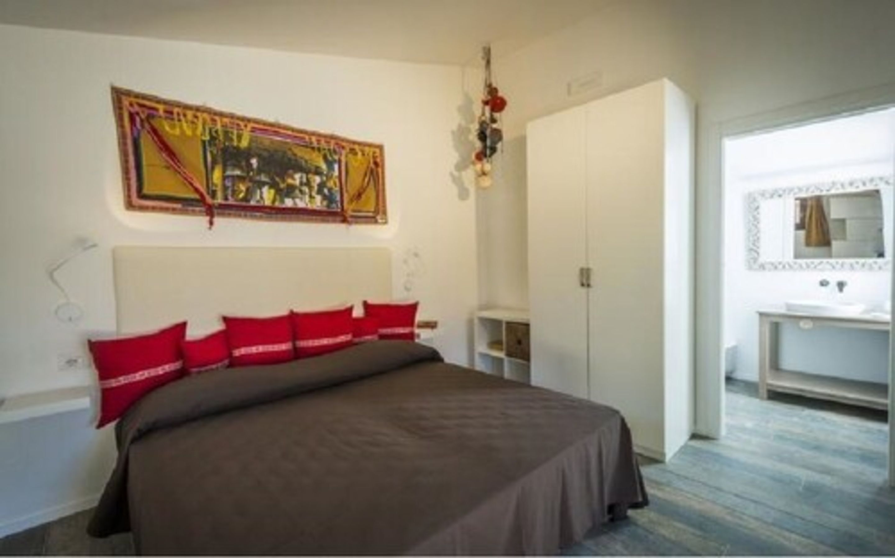 A bedroom with a large bed, a wardrobe, a mirror, and a painting on the wall.