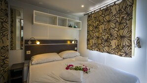 A hotel room with a large bed, a headboard with shelves, a mirror, and a floral curtain. - Tiliguerta Glamping & Camping Village (Muravera)