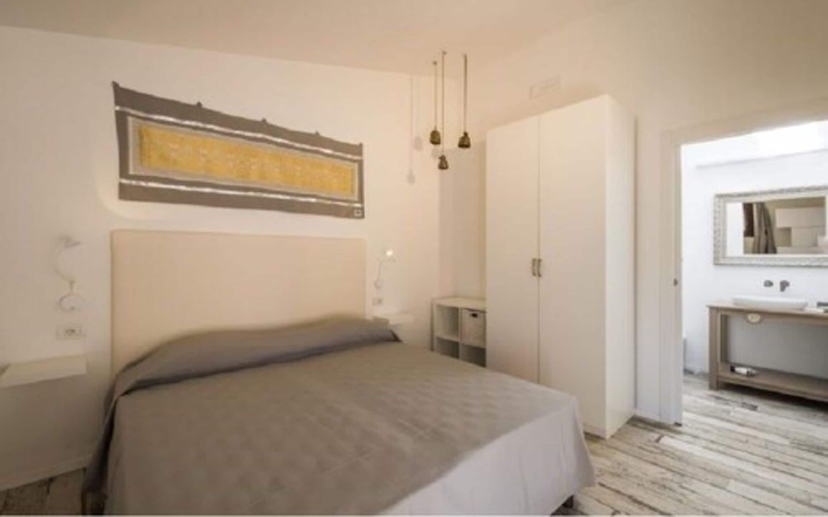Une chambre à coucher comprenant un lit, une table de chevet, une armoire et une salle de bain visible à travers une porte ouverte.