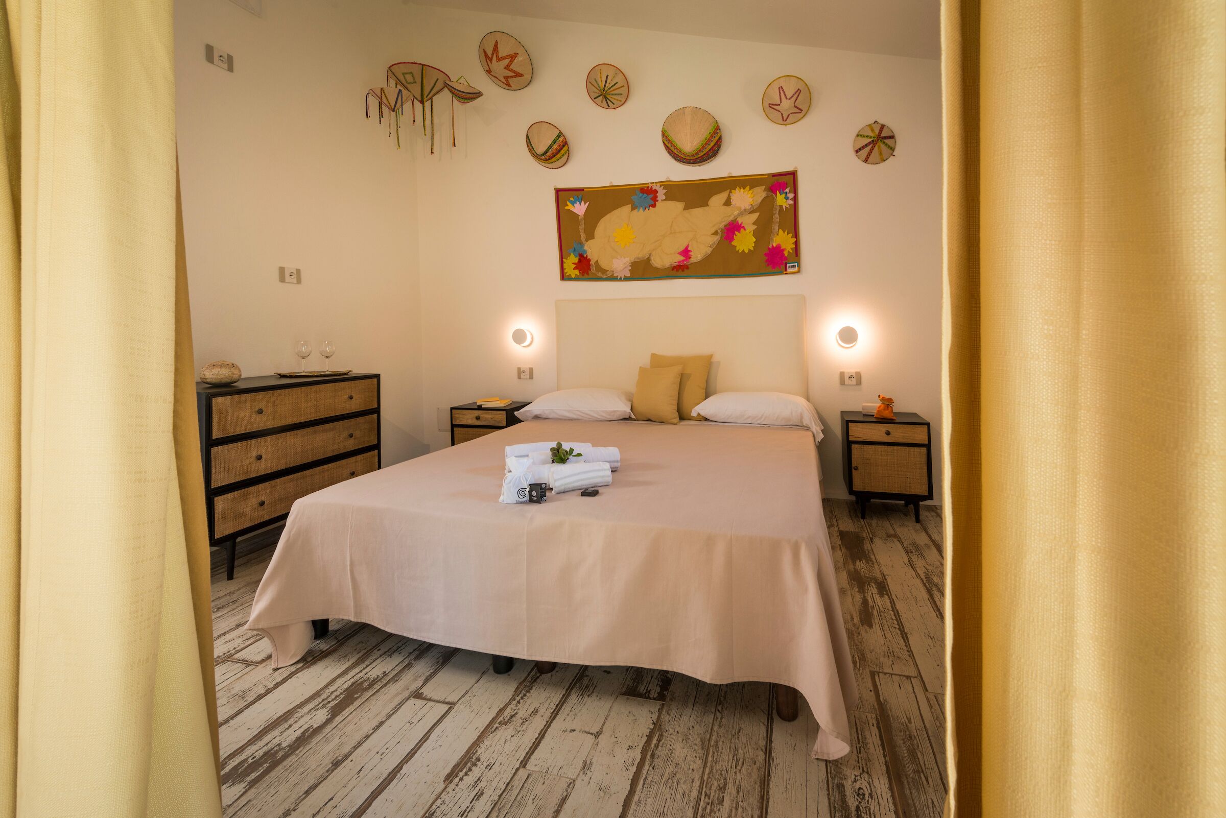 Un dormitorio ordenado con una cama grande, mesitas de noche, un aparador y una pared decorada con arte tribal.