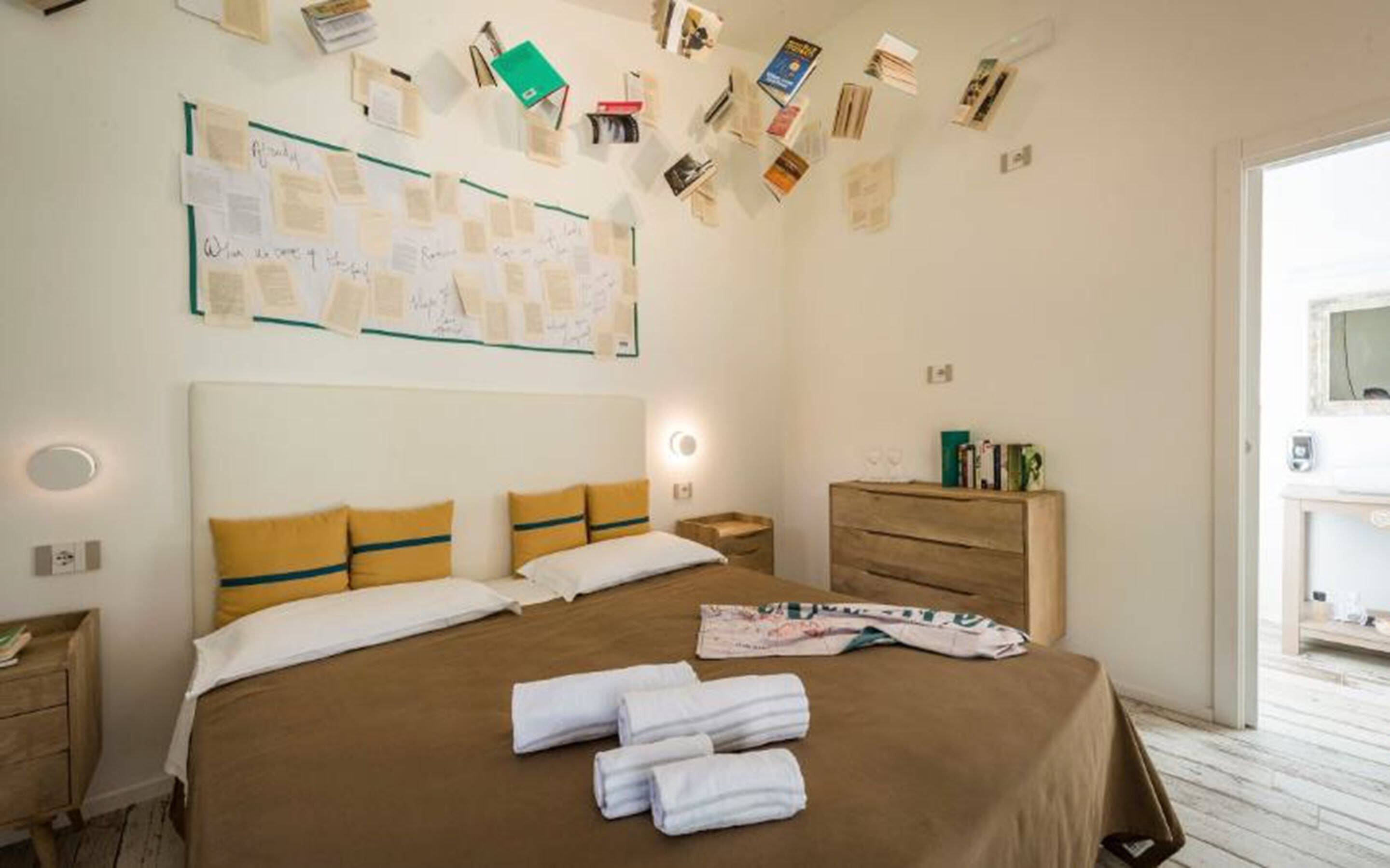 A neatly arranged hotel room with a large bed, a wooden dresser, and a wall with papers and books.