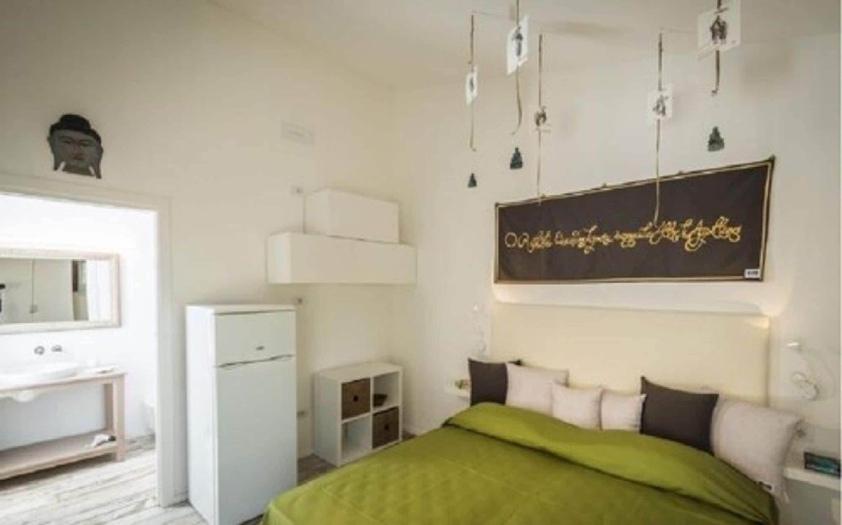 Une chambre à coucher comprenant un lit, une commode, un miroir, un petit meuble blanc et un luminaire fixé au mur.