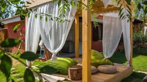 A wooden gazebo with white curtains, green cushions, and a wooden stool. - Tiliguerta Glamping & Camping Village (Muravera)