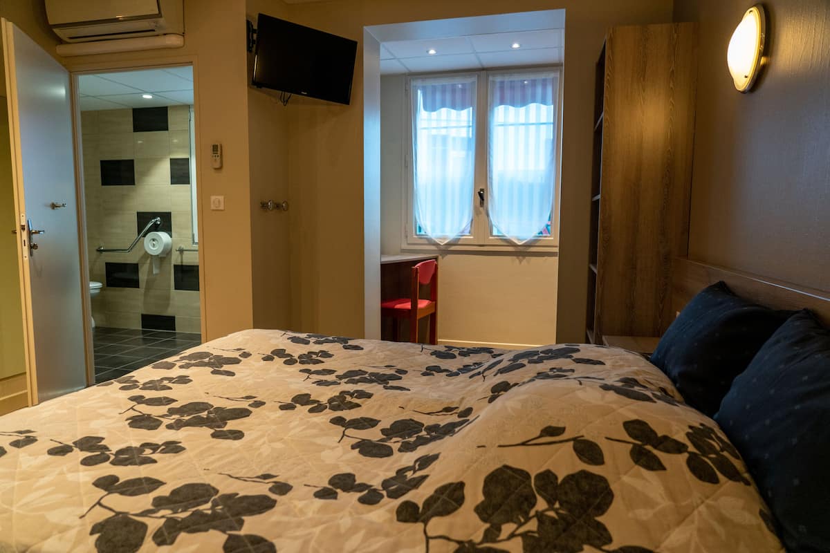 Un dormitorio con cama, ventana con cortinas, televisor y un armario de madera.