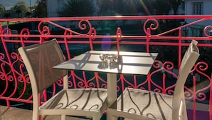 A balcony with a table and chairs, a clear view of the sun, and a building in the background.