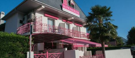 Un hotel con fachada rosa, un balcón con barandillas decorativas y un cartel que indica que es un hotel y restaurante.