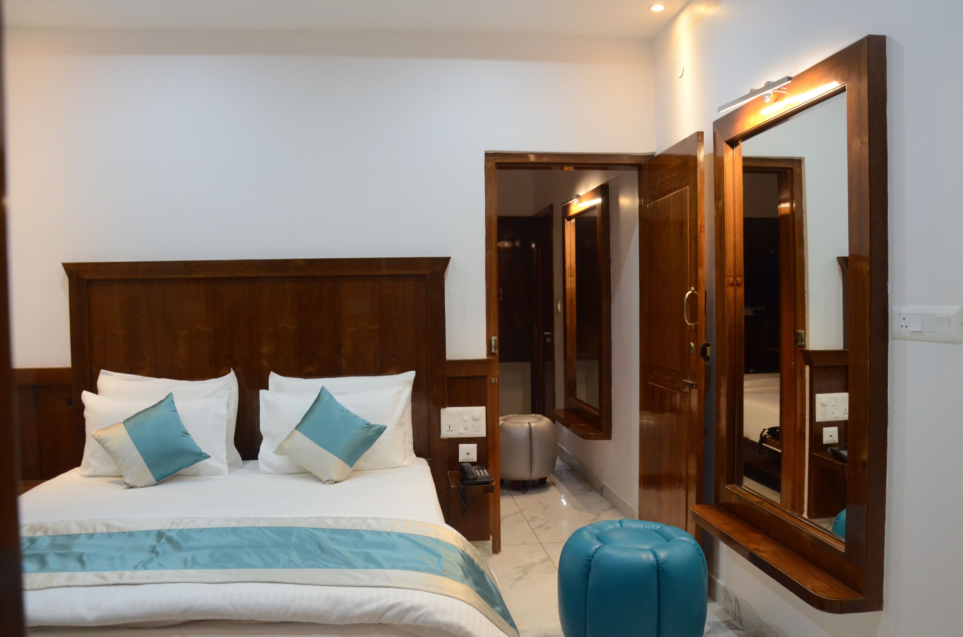 Habitación de hotel con una cama, un armario, un espejo y un taburete pequeño.
