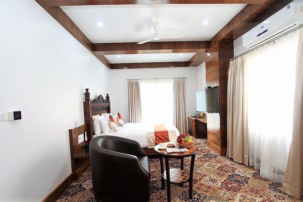 A hotel room with a bed, a desk, a chair, a small table with fruit, a television, and an air conditioning unit.