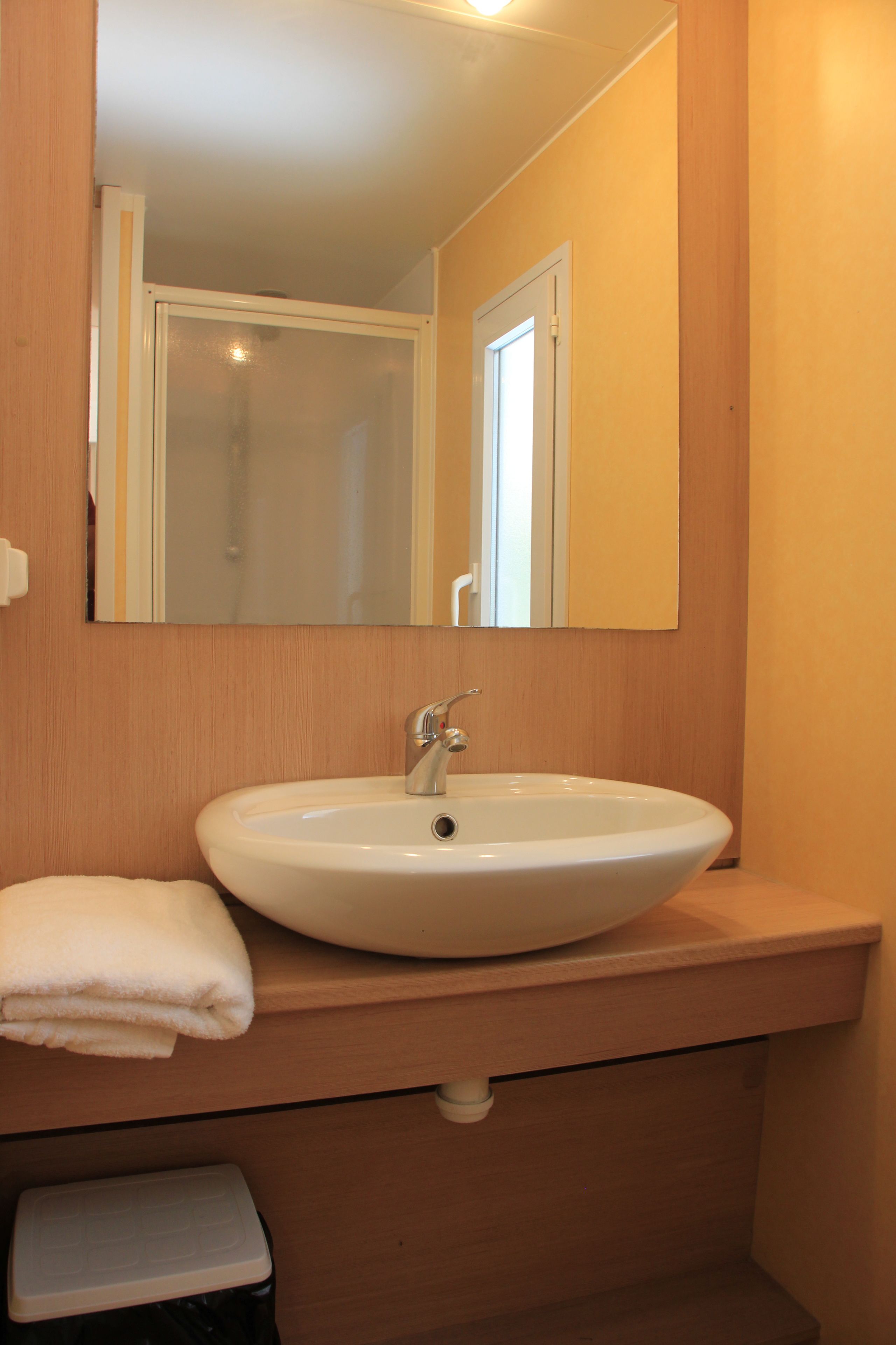 Un baño con lavamanos blanco, espejo y tocador de madera.