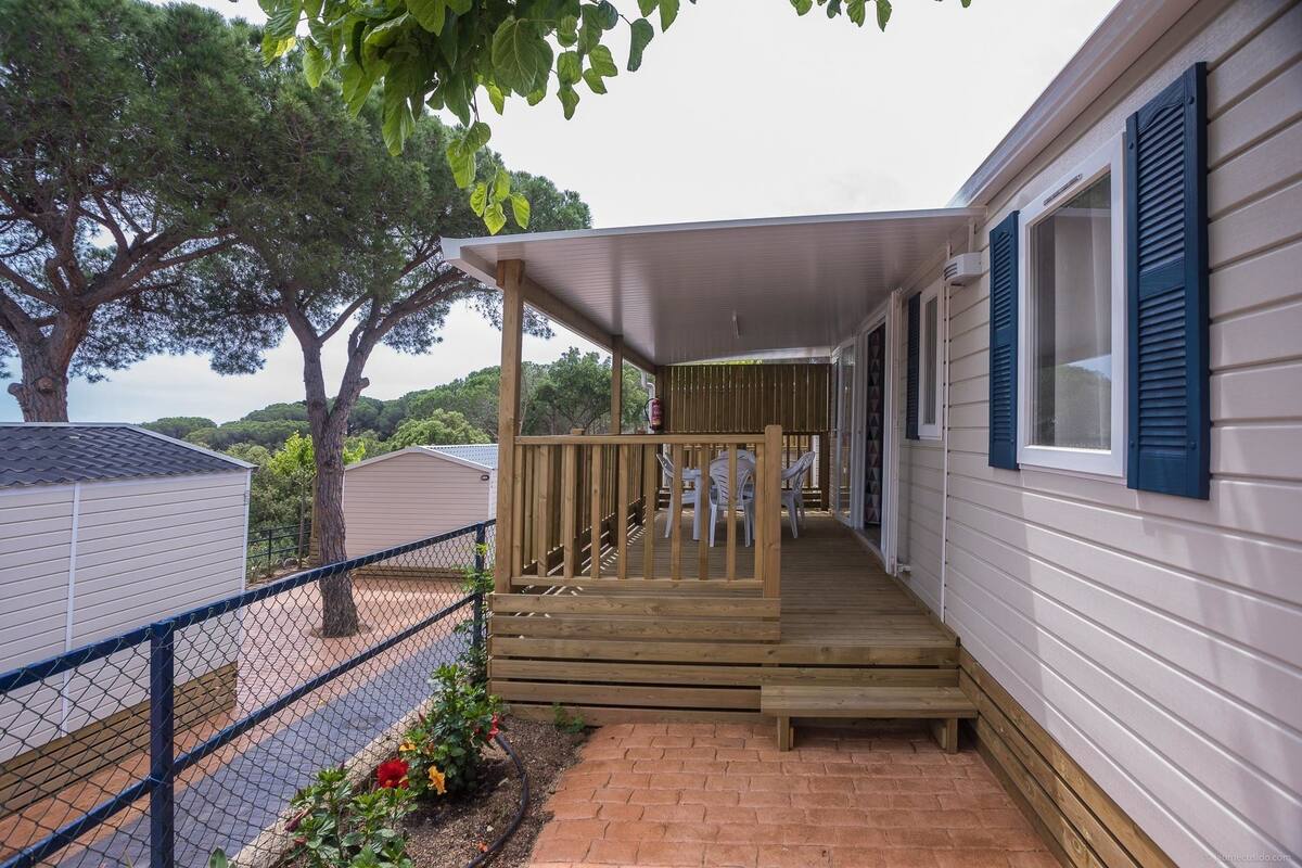 A covered porch with a wooden railing, a brick pathway, and a chain-link fence.