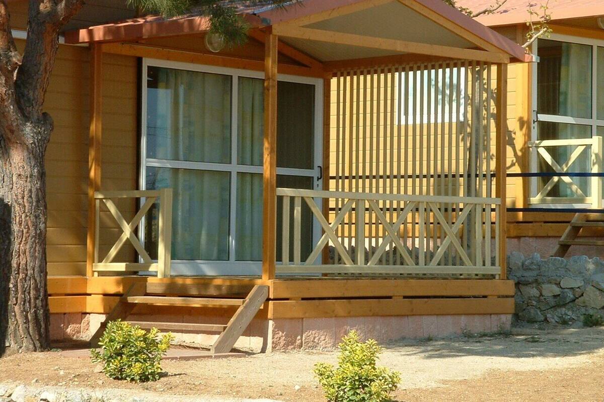 A wooden cabin with a porch, large windows, and a stone foundation.