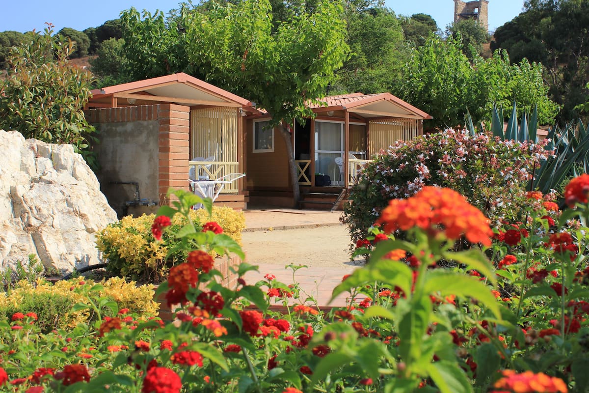 A bungalow-style hotel with a patio area, surrounded by lush greenery and flowering plants.