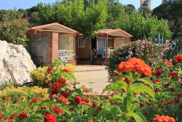 A bungalow-style hotel with a patio area, surrounded by lush greenery and flowering plants.