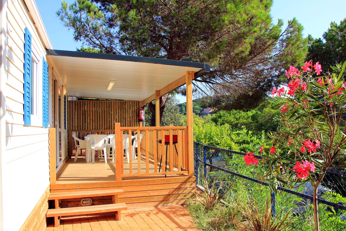 A wooden deck with outdoor furniture, a covered area, and a view of greenery and trees.