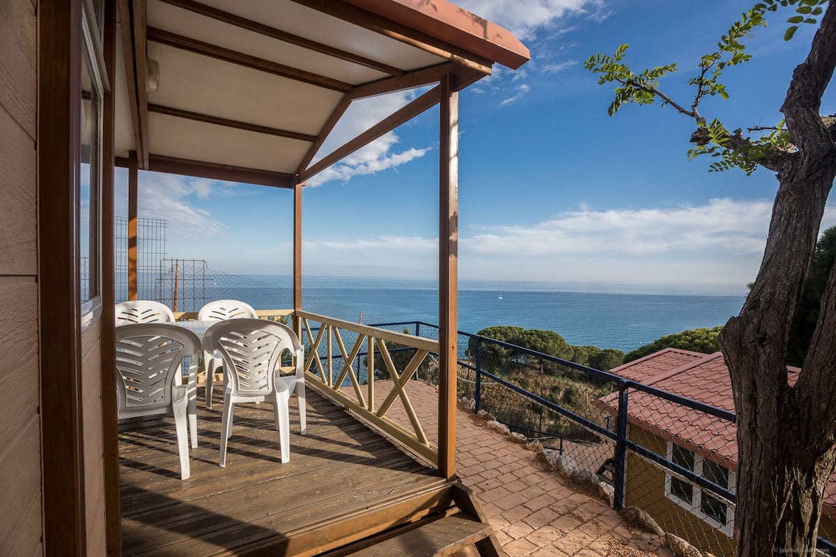 A wooden deck with white plastic chairs, overlooking a coastal view.