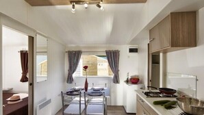 A compact kitchen with a dining area, a window with curtains, and a view of the outside. - Camping Roca Grossa (Calella)