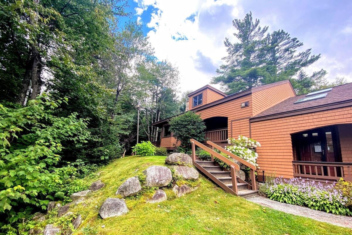 A two-story house with a wooden deck and a stone staircase leading to the entrance.