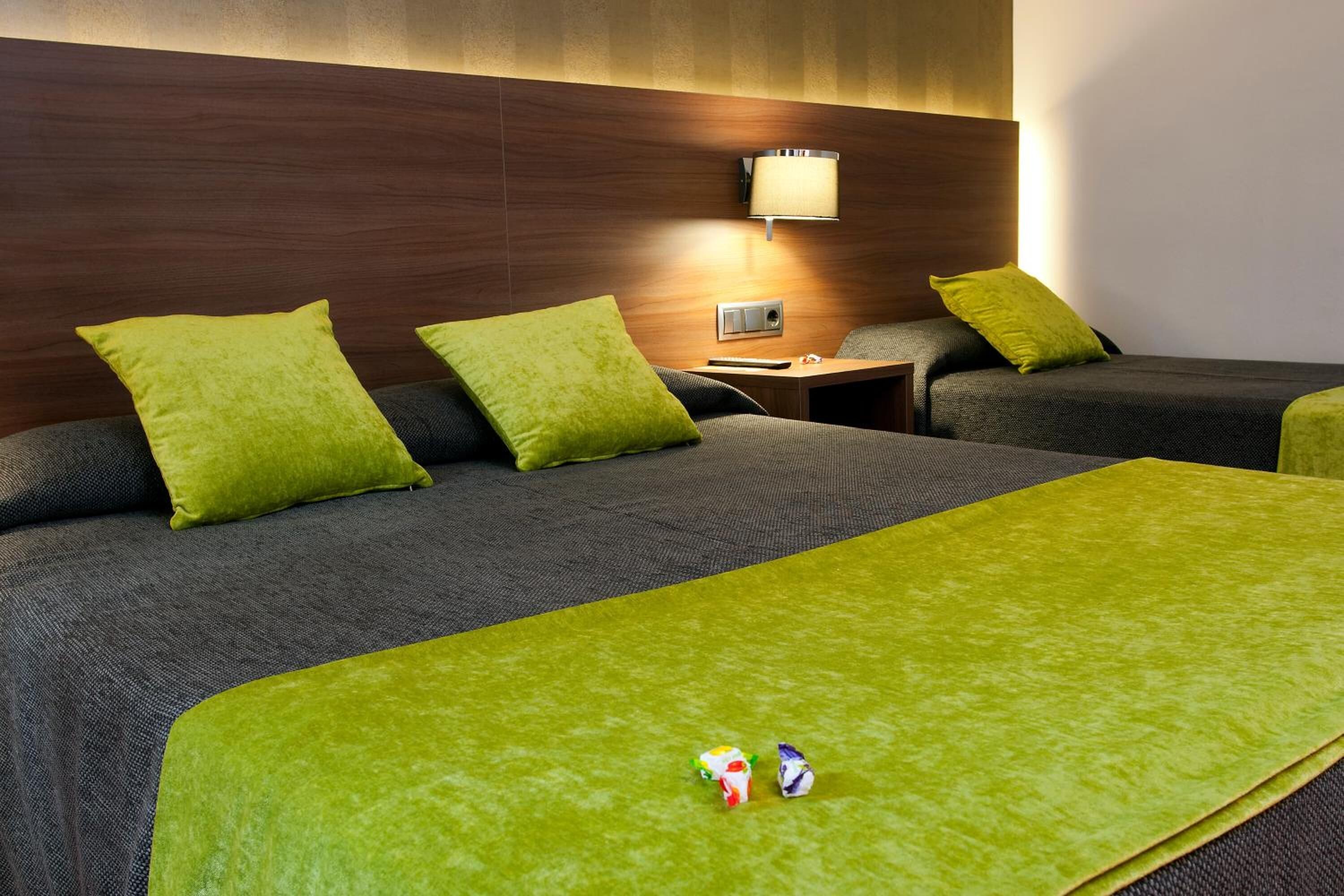 A hotel room with a large bed, two pillows, a nightstand, a lamp, and a small table.
