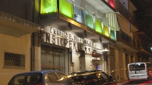 Un immeuble à plusieurs étages, avec une enseigne lumineuse et bien visible indiquant « PENIBIO EL PEKI NAIRE », et un magasin dont la devanture est visible au rez-de-chaussée.
