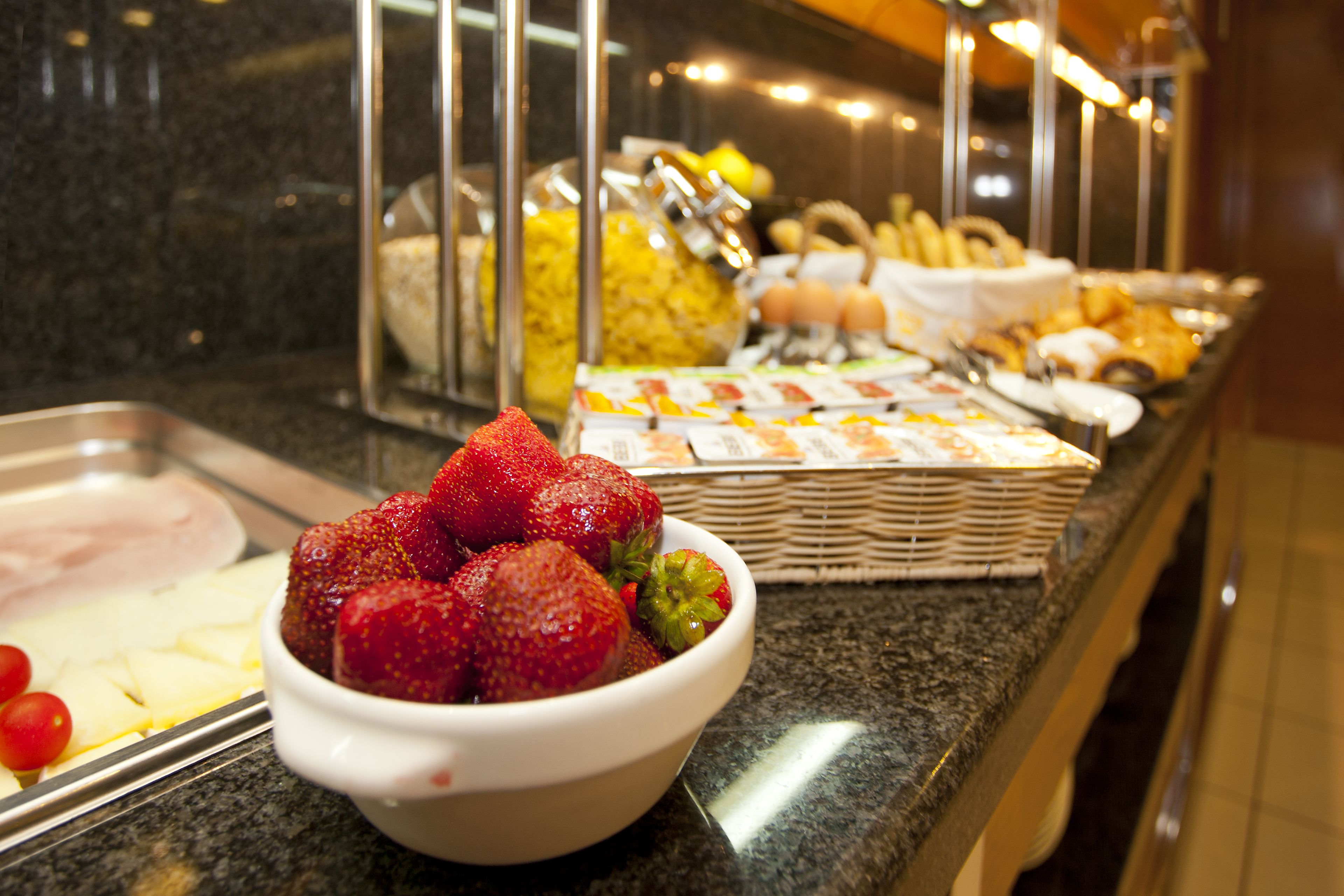 Un buffet proposant une variété de plats, notamment un saladier de fraises, un plateau d’œufs et un panier de viennoiseries.