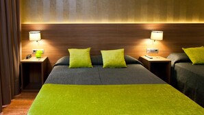 Une chambre d’hôtel avec deux lits, chacun recouvert d’une couverture verte et doté d’un oreiller, ainsi que de deux lampes de chevet et d’une tête de lit en bois.
