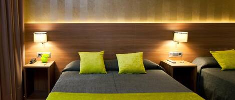 Habitación de hotel con dos camas, cada una con cubrecama y almohada verde, dos lámparas de noche y un cabecero de madera.